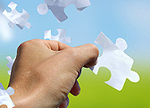 Hand fitting a puzzle piece into place against a blue sky